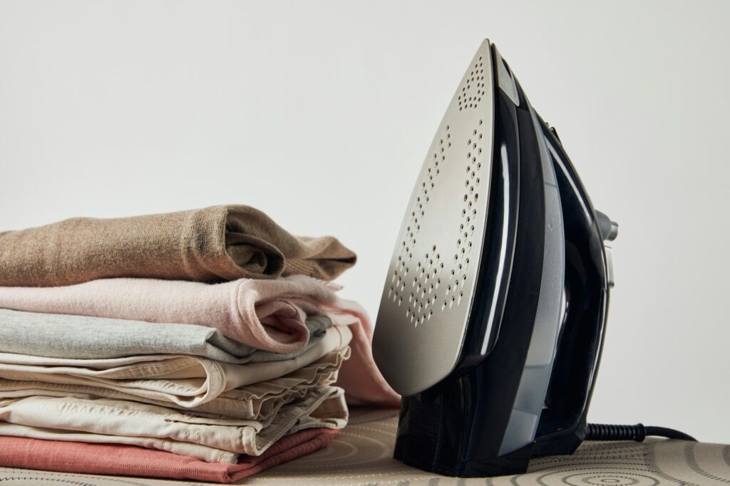 Iron and folded ironed clothes on ironing board isolated on grey